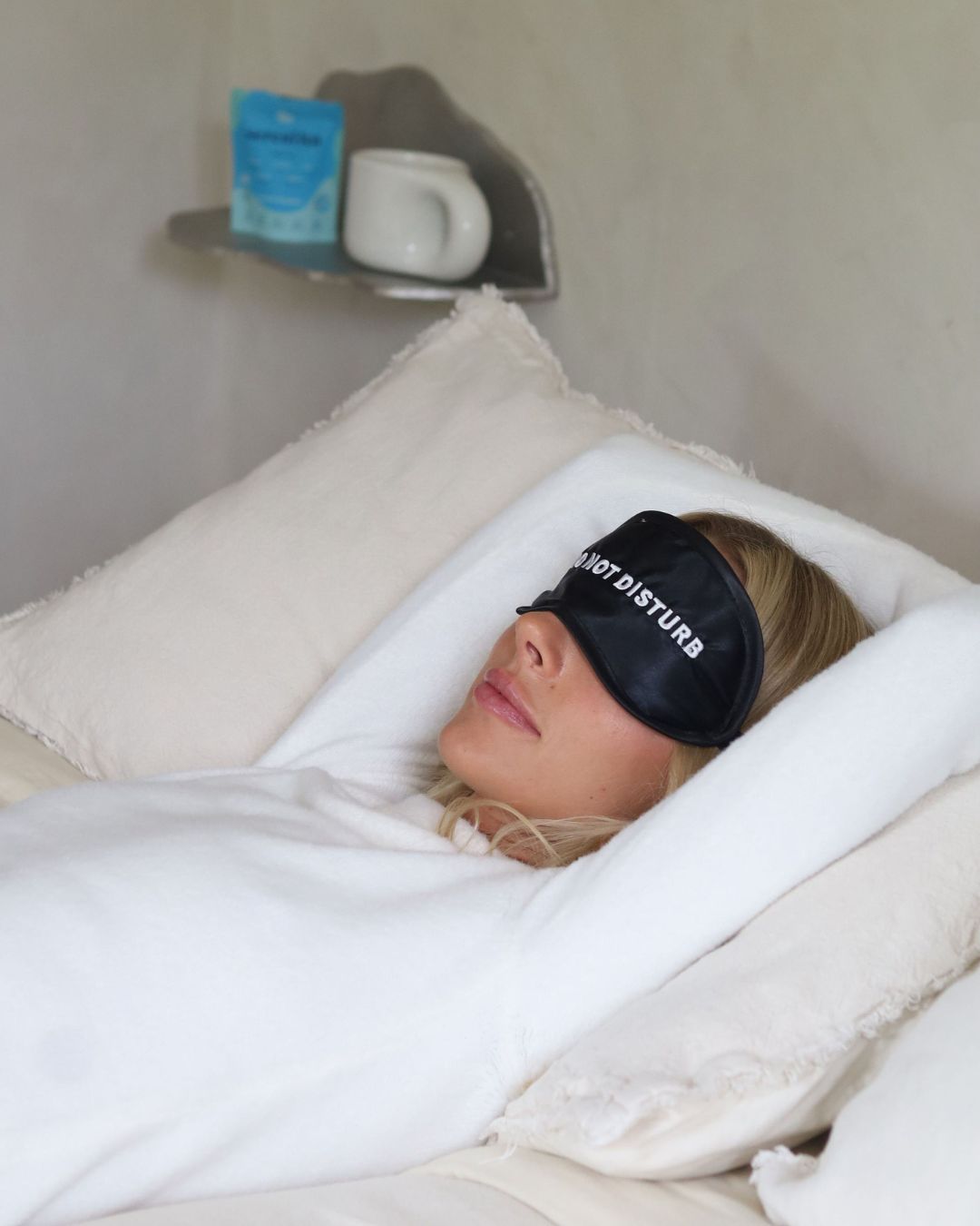 Mujer descansando en la cama con antifaz, con un envase de SereniTEA y una taza en la repisa