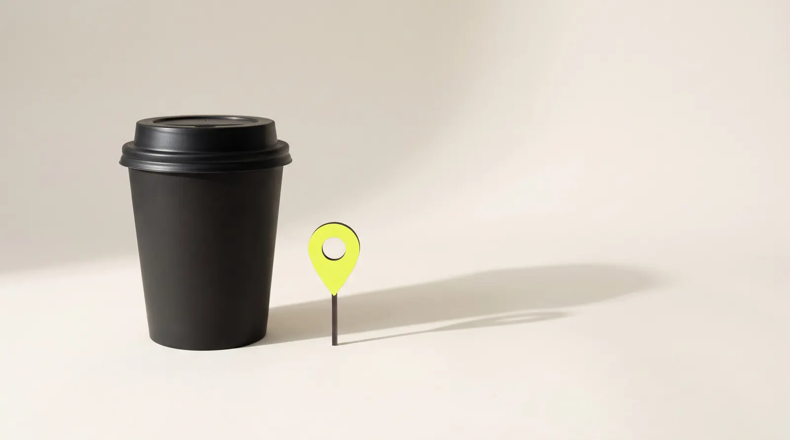 Black takeaway coffee cup with a lid next to a small lime map pin, like a café marked on the map.