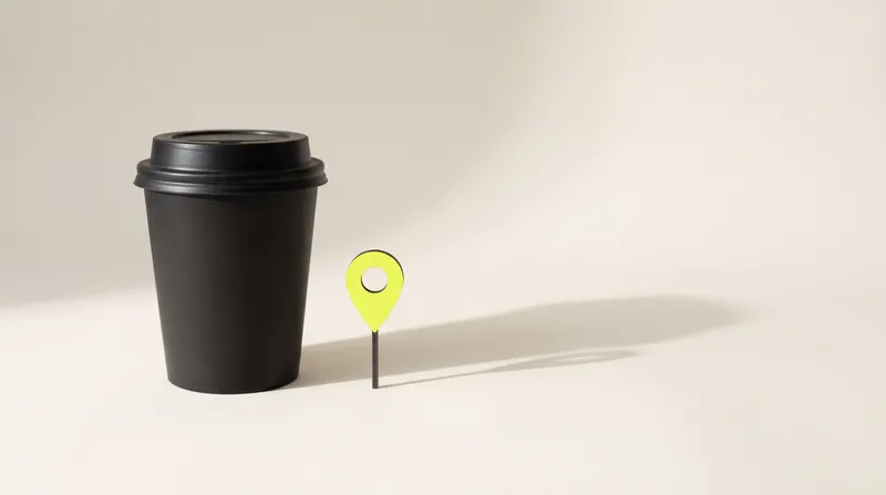 Black takeaway coffee cup with a lid next to a small lime map pin, like a café marked on the map.