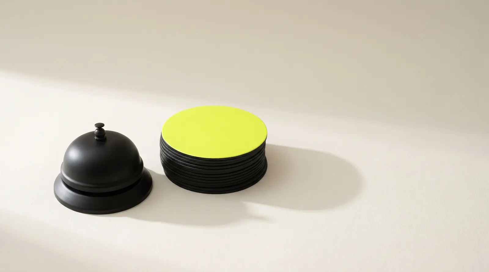Black service bell next to a stack of black coasters with a lime one on top: guests who come back.