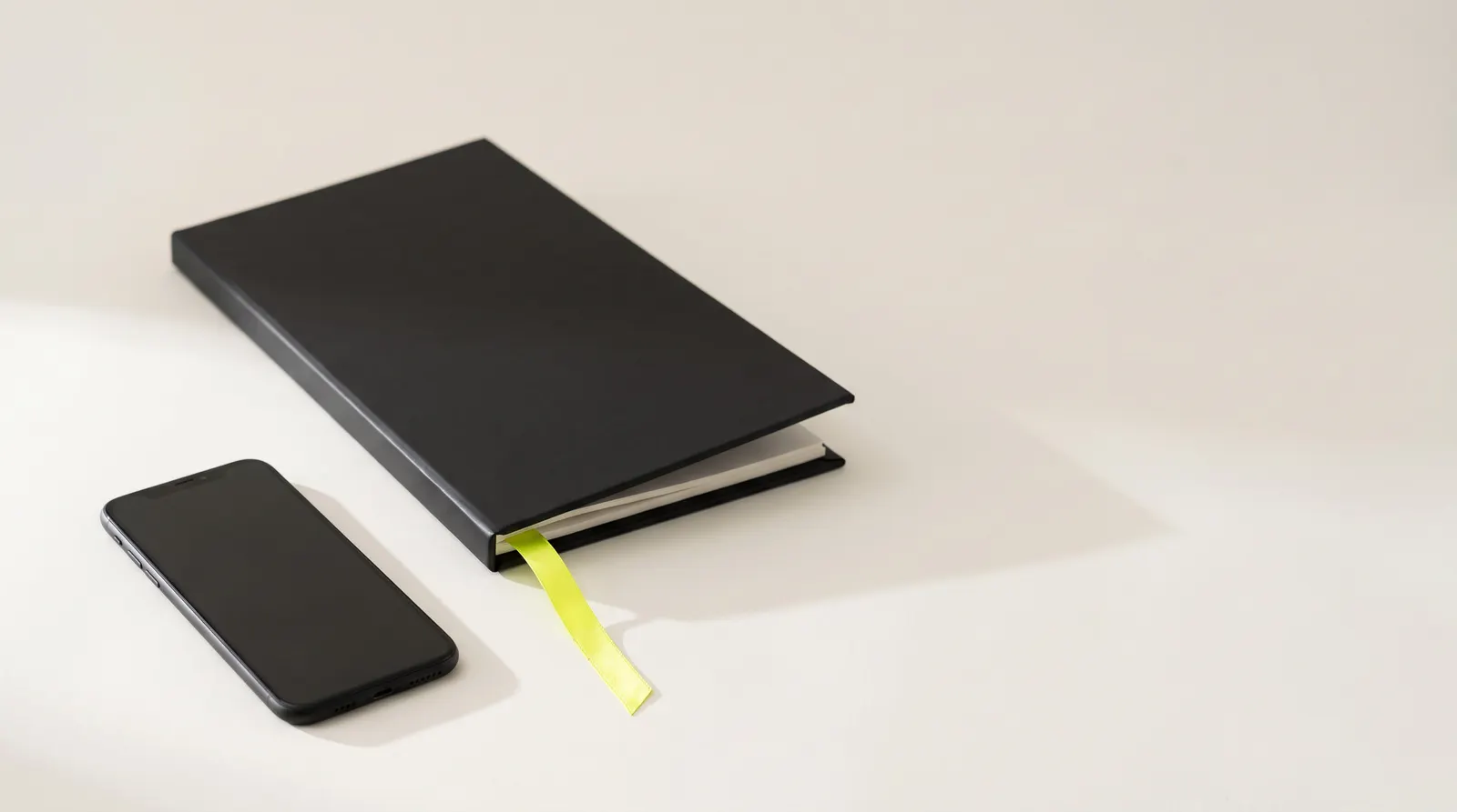 Closed black menu with a lime ribbon next to a black phone with a dark screen: the menu on paper and on the phone.