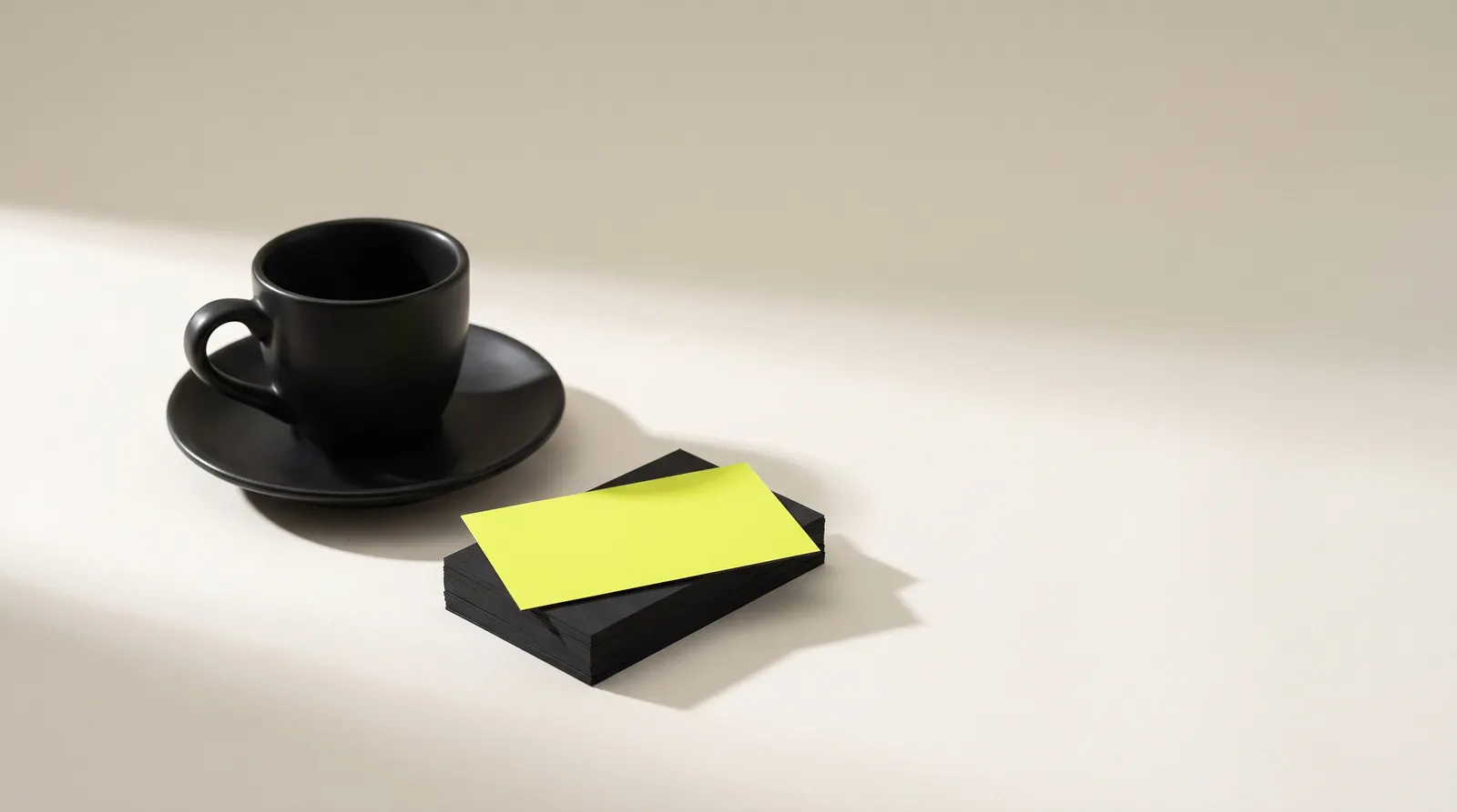 Black espresso cup on a saucer next to a stack of black cards with a lime one on top, like a café loyalty program.